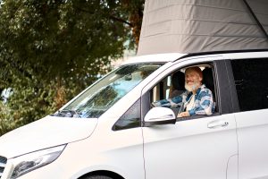 Happy older man traveler driving camper van sitting inside, campervan rentals.