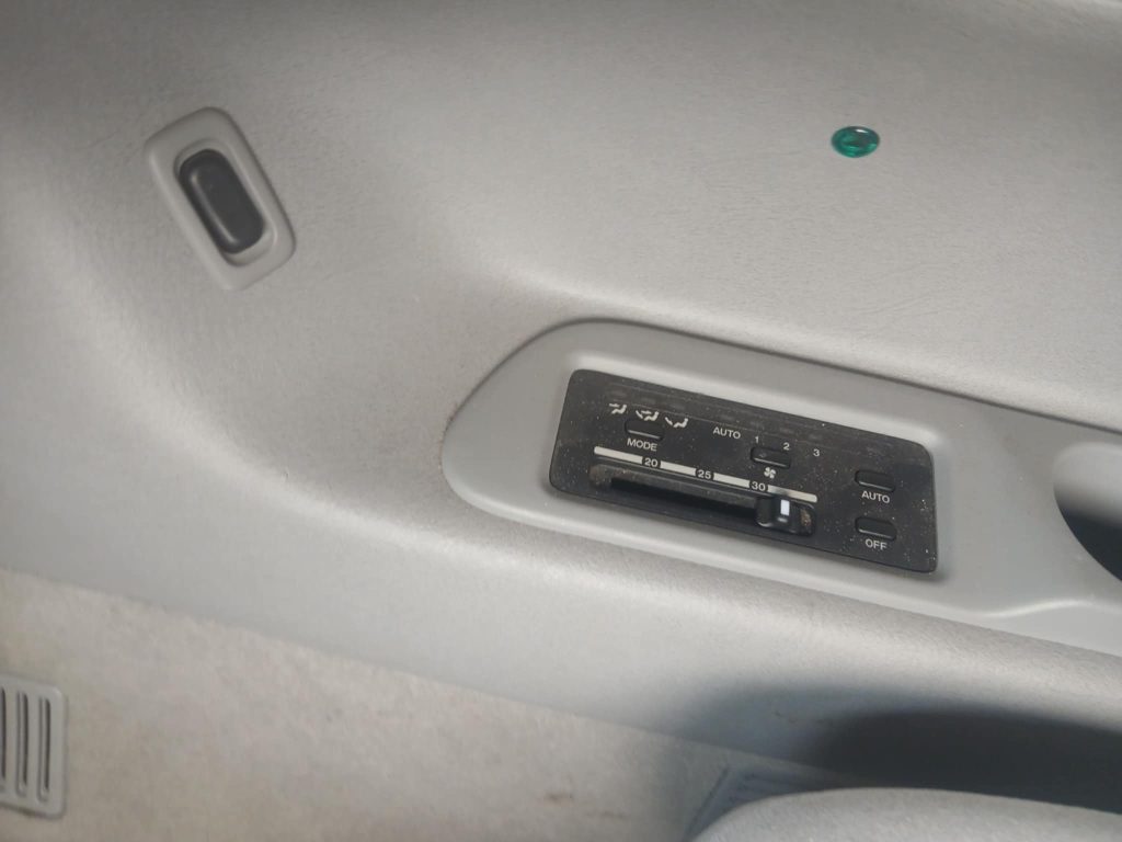 Close-up of the rear passenger climate control panel in a Mazda Bongo, with slider and buttons for adjusting temperature, airflow mode, and fan speed, set into the light grey trim of the interior side panel.