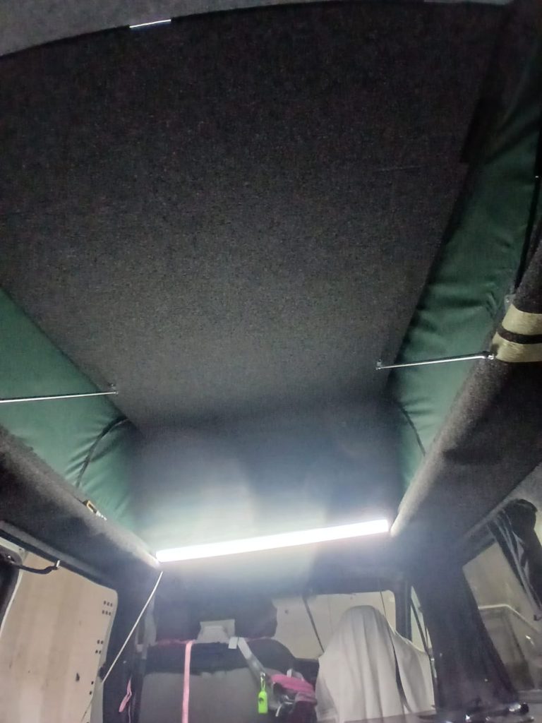 Interior view of newly installed pop-top roof on a Vauxhall Vivaro, showing carpet-lined upper bed platform and green canvas sides fitted by Kinmel Campers.