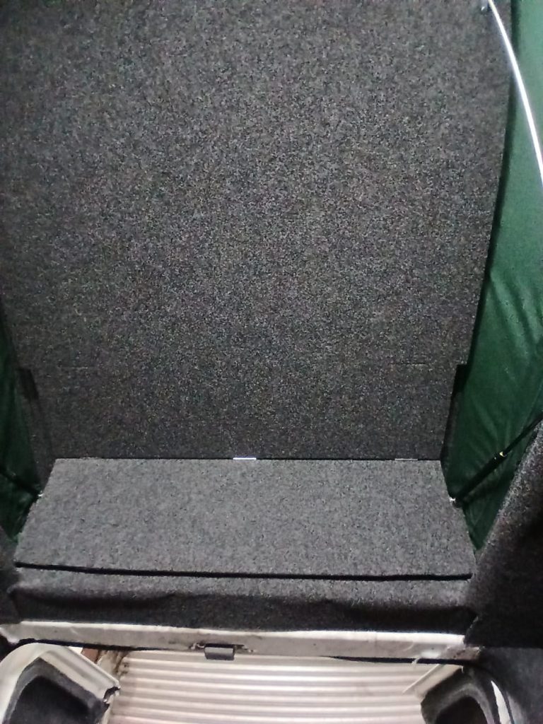 Rear-facing view of the bifold bed platform and carpeted lining fitted neatly into a Vauxhall Vivaro undergoing campervan conversion at Kinmel Campers.