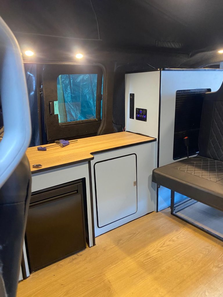 Custom kitchen with hob, sink and storage in handcrafted VW T5 camper build.