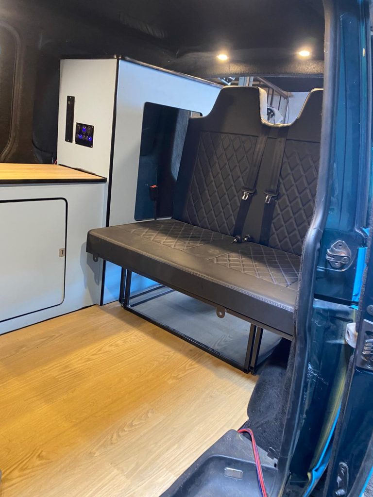 Rock and roll bed in sleep position, upholstered to match VW T5 interior.