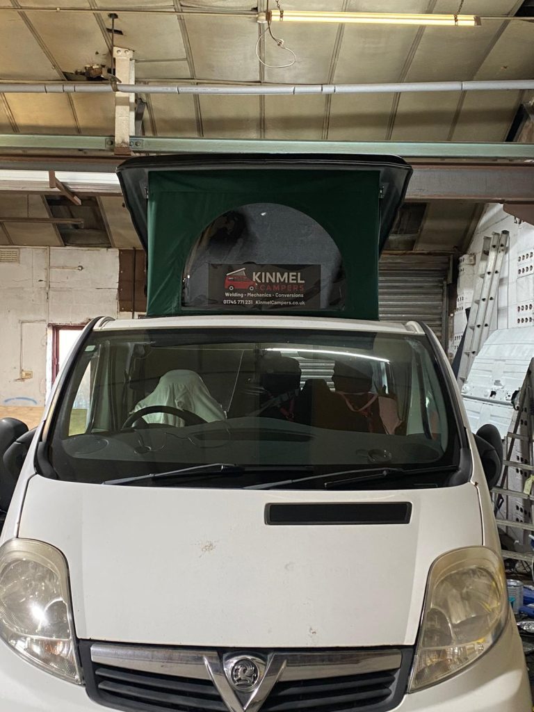 Front view of a Vauxhall Vivaro with the newly installed green pop-top roof raised inside the workshop, showing the completed campervan upgrade
