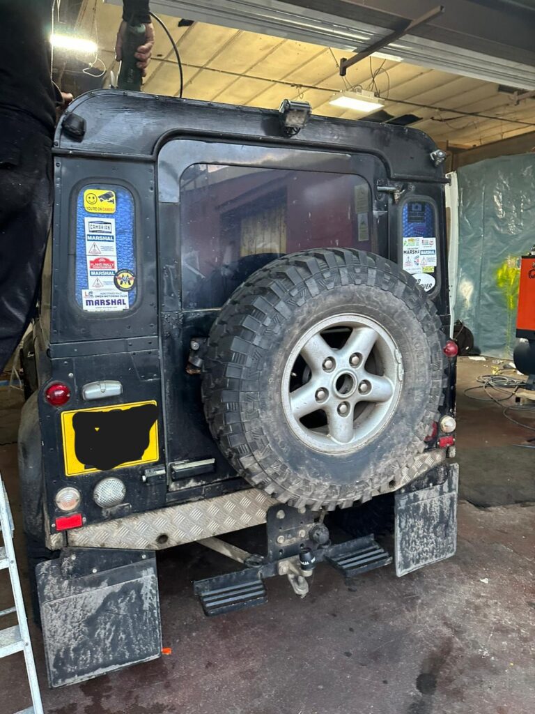 Rear shot of Land Rover Defender with technician preparing the roof area for pop top installation