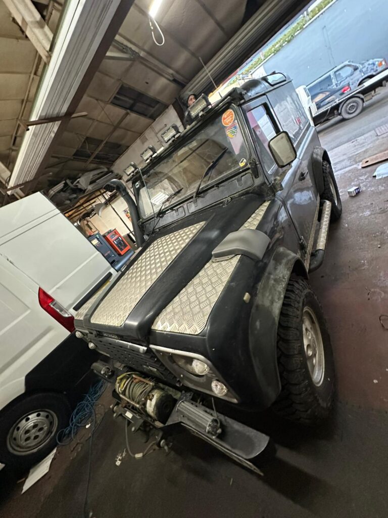 Land Rover Defender with rugged accessories including winch, snorkel, and bonnet checker plating